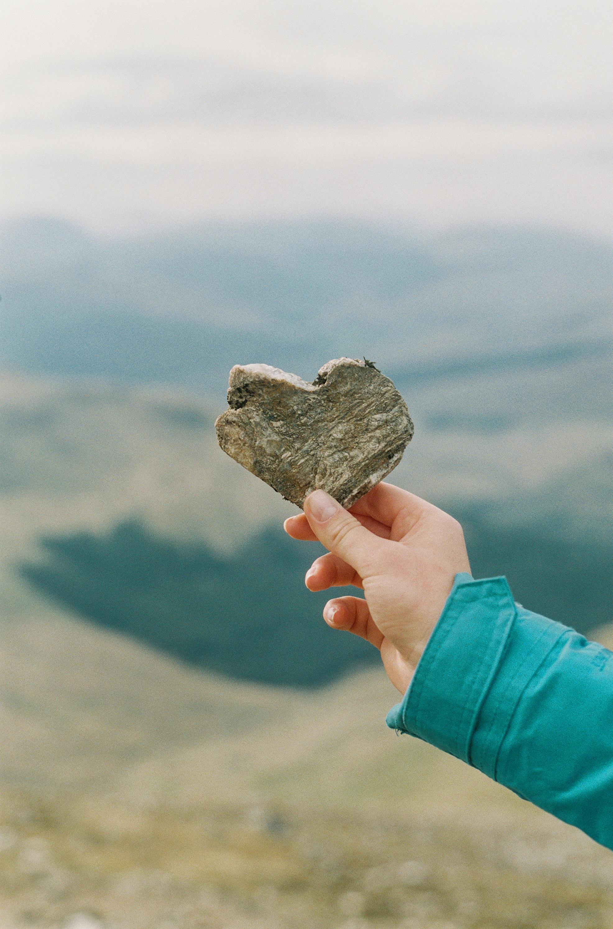 Hand holding a heart-shaped stone by the water symbolizing care and compassion