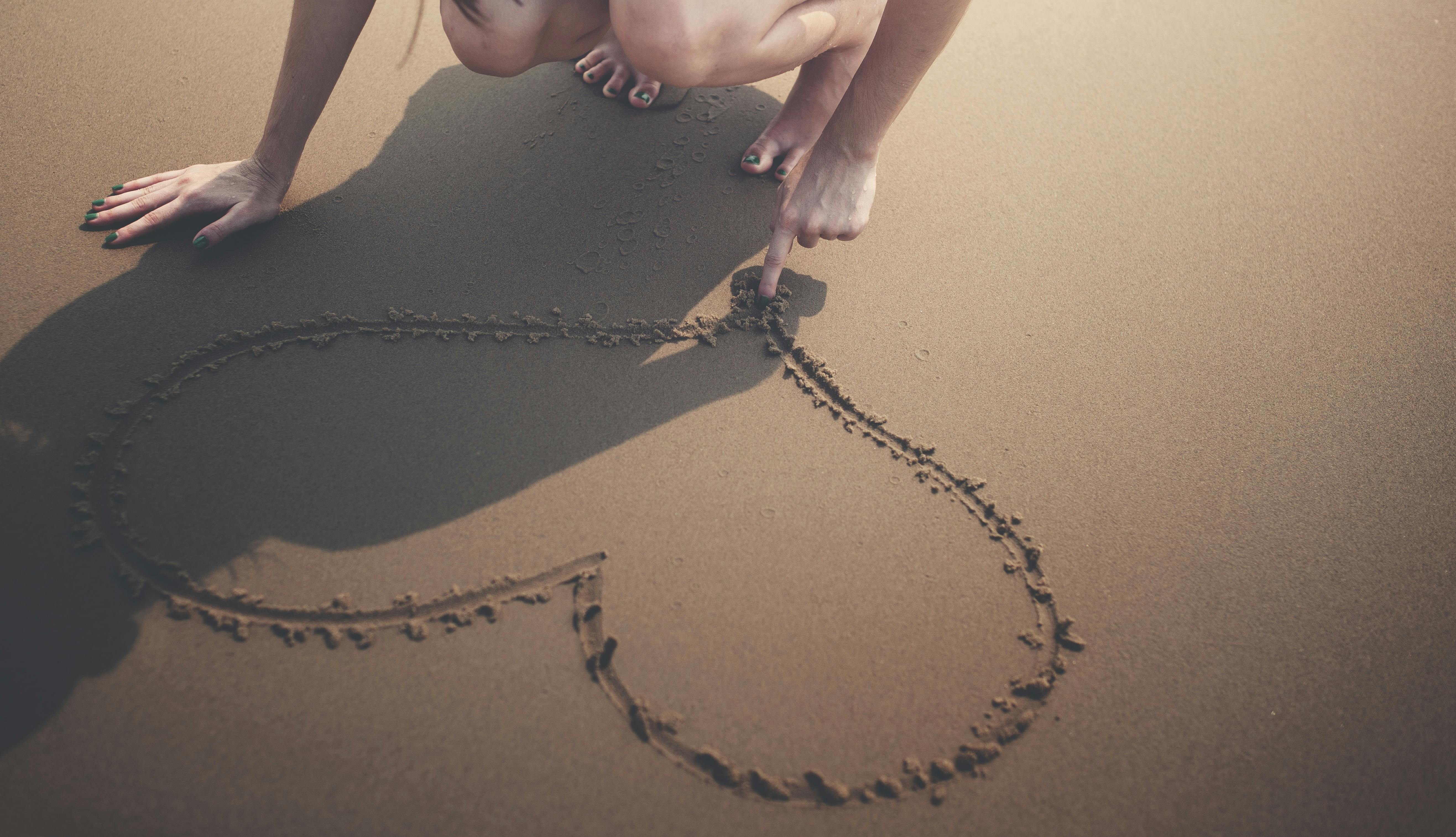 Person drawing a heart in the sand representing community and connection