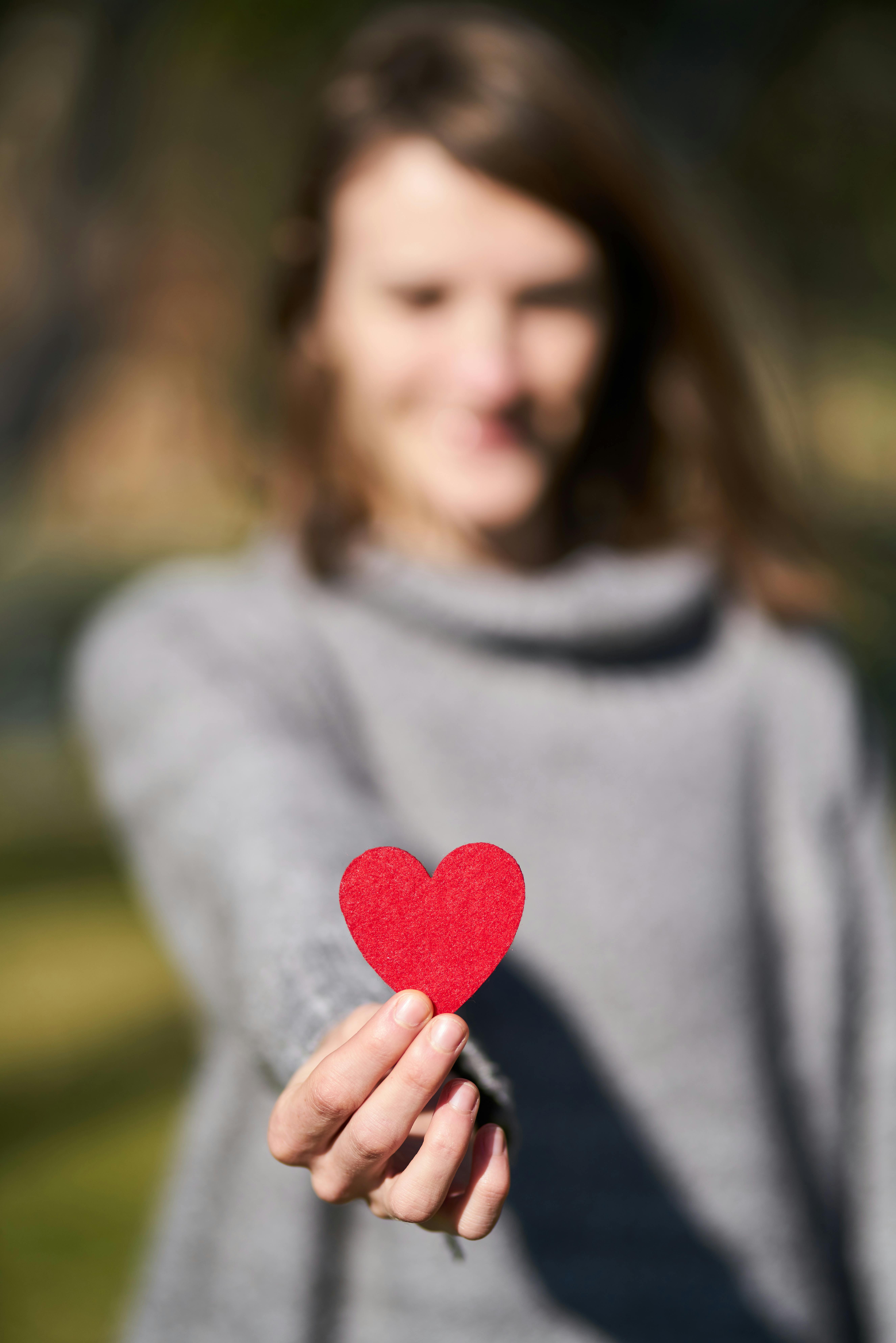 Person holding a red heart toward the camera representing giving and support