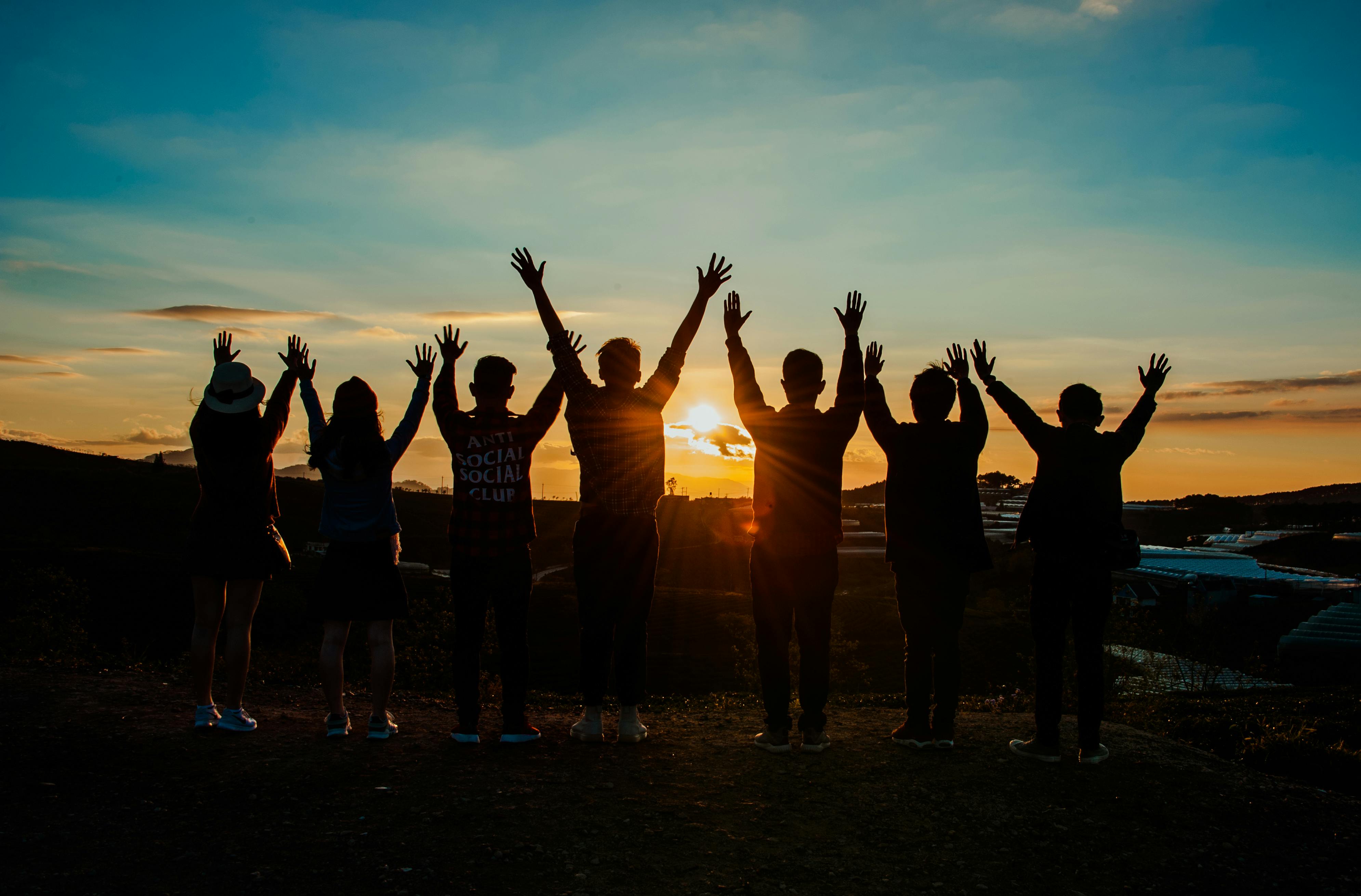 Group of people standing together at sunset with raised hands representing unity and community impact